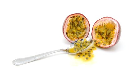 Spoon scooping out pulp and seeds from a purple passion fruit cut in half, on a white backgroundの写真素材