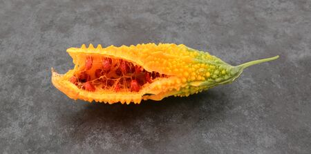 Orange bitter gourd, with ridged flesh, split open to show red seeds, on slate gray backgroundの写真素材