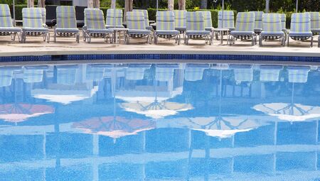Swimming pool with empty chairs and umbrellas reflections