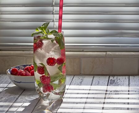 Kitchen counter with glass of fruit infused water and bowl with raspberryの写真素材