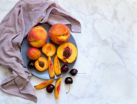 Plate with peaches, apricots and cherries on light marble background. Flat lay, top view.の写真素材