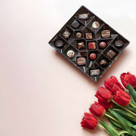 Box of chocolates and red tulips on light pink background. Flat lay, top view.の写真素材