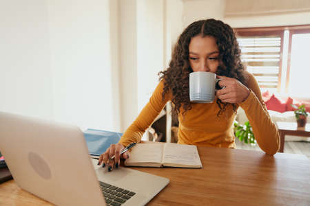 Multi-cultural female working from home, sipping coffee. Young professional remote working with...