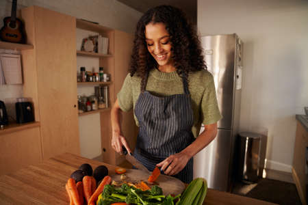 Multi-cultural young female chopping vegetables in modern kitchen, preparing healthy meal at home.の写真素材