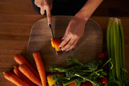 Birds eye view of multi-cultural female chopping vegetables on wooden chopping boardの写真素材