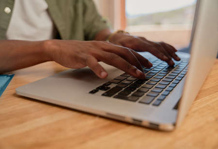 Young adult black male typing on laptop. Close up of hands, working from home, sitting at modern styled kitchen counter.の写真素材