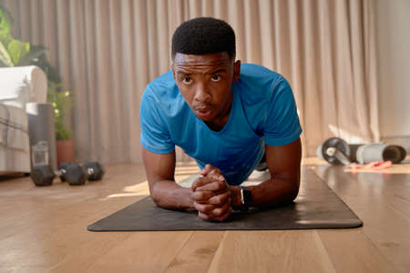 Young African American male working out at home holding a plank position on a yoga mat