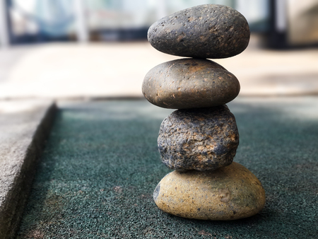 Four stones stacking up in balance on greenish floor.