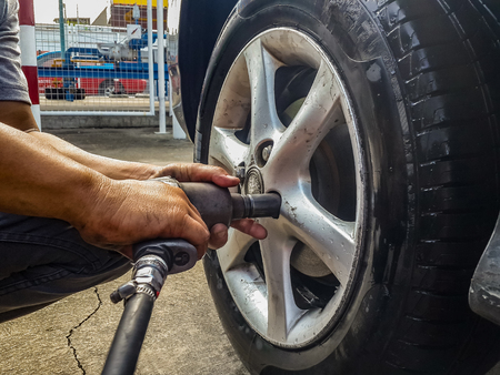 asian man hands holding pneumatic wrench screwing wet car tire for replacement after fixing air leak at garage.の写真素材