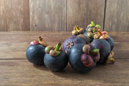 Closeup of several purple mangosteens various angles on wooden table. Mangosteen is native plant to Sunda Islands and the Moluccas of Indonesia. Grows in tropical areas. Designated as Queen Of Fruits.の写真素材