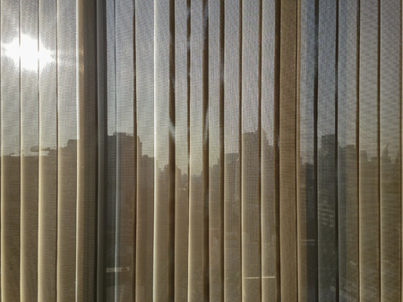 beige, brown color semi transparent vertical blinds with blurred afternoon sun and business district...