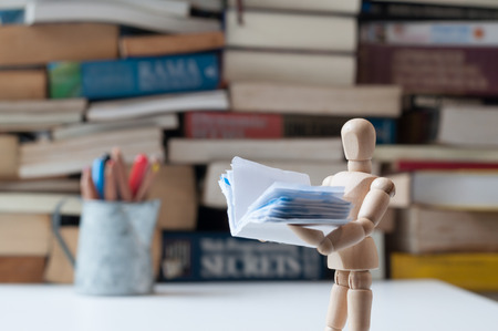 Wood manikin reading miniature book with blurred book pile and blurred pencil cup in background....