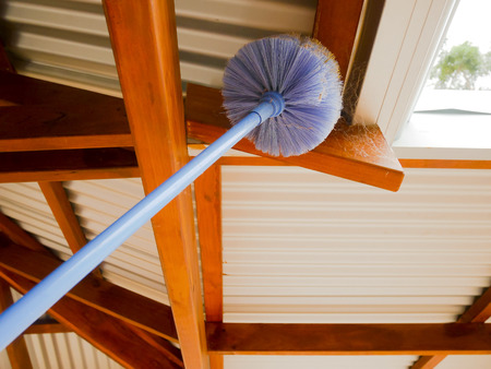 Cobweb brush sweeping spiderweb under the roofの写真素材