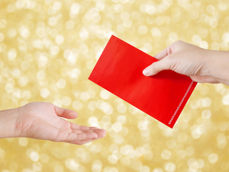 Woman's hand giving red packet on Chinese New Year on gold bokeh backgroundの写真素材