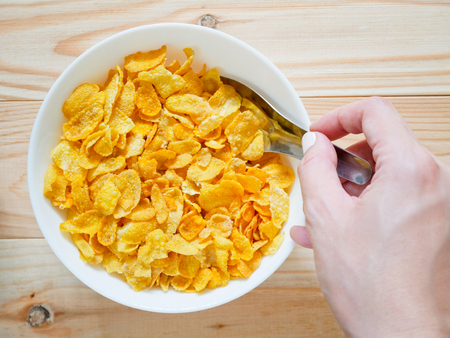 Golden cornflakes cereal on wooden table with hand holding spoonの写真素材