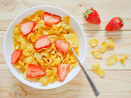 Golden cornflakes cereal with strawberries on wooden background. Top view.の写真素材