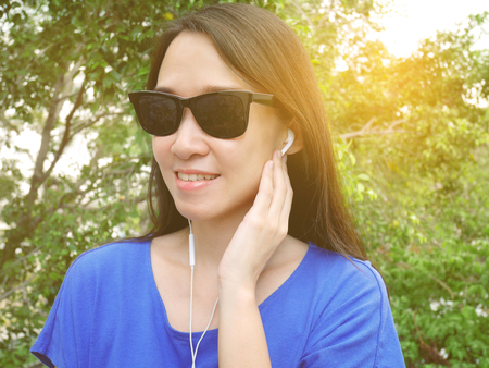 Young asian woman listening to music from earphones in the park