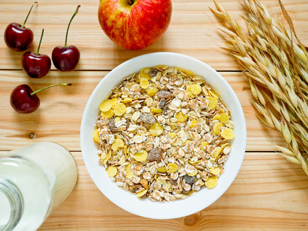 A Bowl of muesli breakfast with fresh fruits, a bottle of milk and dried oat on wooden table. Top view.の写真素材