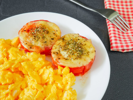Roasted tomatoes with mozzarella cheese and scrambled eggs for breakfastの写真素材