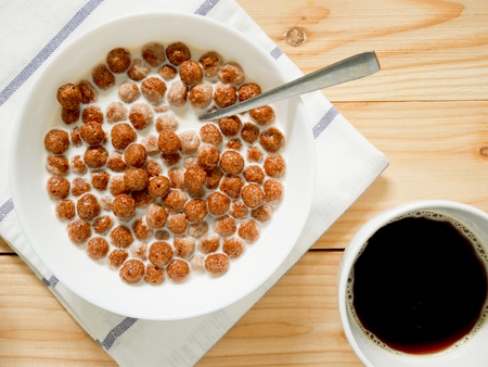 Chocolate cereal balls with milk in a bowl and a cup of coffee on wooden background. Healthy breakfast concept. Top view.の写真素材