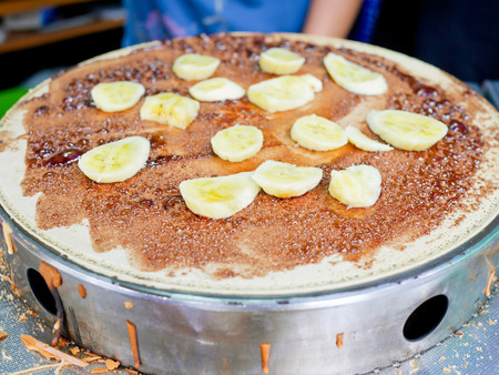 Crepe filling with chocolate sauce and banana being cooked on crepe makerの写真素材