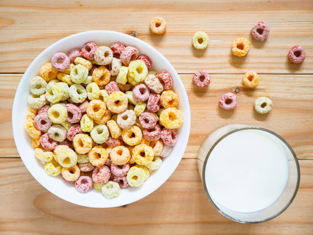 Colorful fruity breakfast cereal in a bowl with a glass of milk on woodenの写真素材