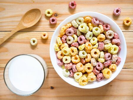 Colorful fruity breakfast cereal in a bowl with a glass of milk on woodenの写真素材