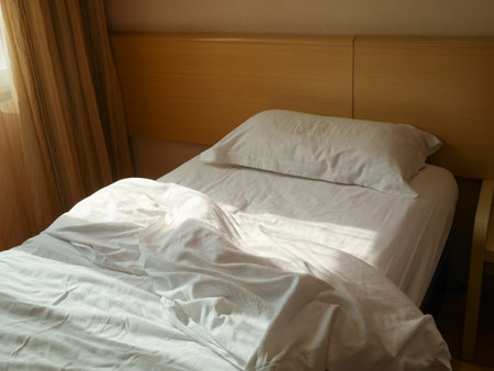 Unmade bed with crumpled duvet, bed sheet and pillow at the hotel in the morningの写真素材