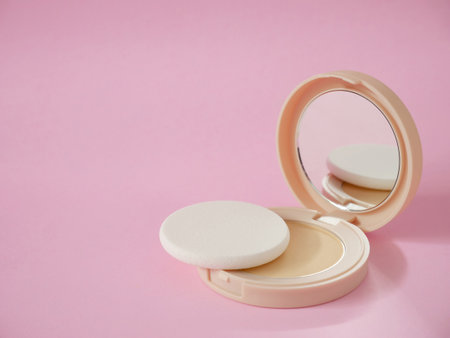 Face powder with sponge in beige case on pink background with copy space. Powder foundation, compact powder make-up.の写真素材