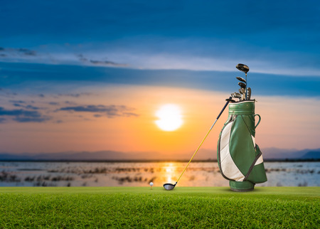 Golf bag, ball, putter and driver  (wood no 1) on green sunset as background.の写真素材