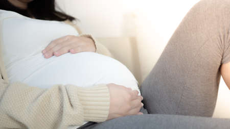 Happy pregnant woman touching her beautiful belly sitting in the bed. Pregnancy, motherhood, and...
