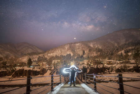 A man in a wetsuit stands on the bridge and looks at the milky way in the mountains.の写真素材