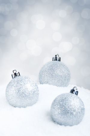 Silver Christmas baubles on snow with defocused silver and white lights in the background. Shallow depth of field.の写真素材