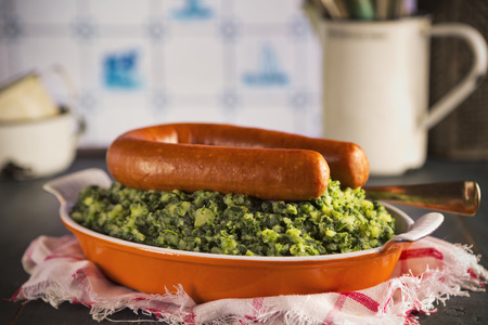 A rustic kitchen with a dish with 'Boerenkool met worst' or kale with smoked sausage, a traditional Dutch meal. With typical Dutch Delft blue tiles on the wall in the background.の写真素材