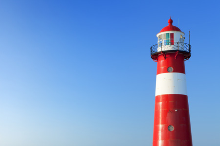 A red and white lighthouse at sea under a clear blue sky. Photographed near Westkapelle in Zeeland, The Netherlands.の写真素材