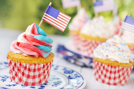 Red-white-and-blue cupcakes with American flags on an outdoor table.の写真素材