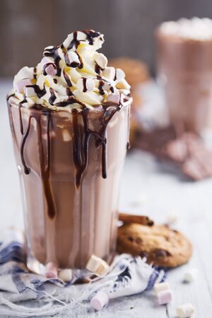A messy glass with hot chocolate, whipped cream, marshmallows and chocolate chip cookies.の写真素材