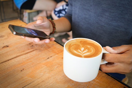 woman use mobile phone with coffee cup and chocolate cake on wood table in coffee shop.の写真素材