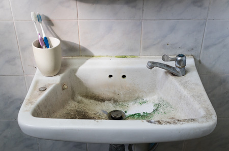 dirty sink with toothbrush and tap in dirty bathroom.の写真素材