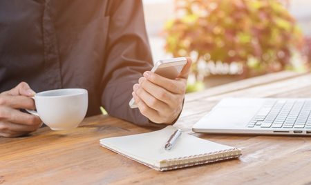Close up businessman using mobile phone and holding coffee cup.の写真素材
