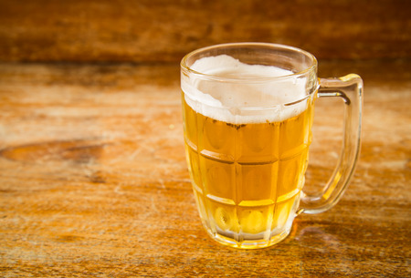 Cold beer into a glass placed on a wooden background.
