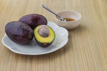 Avocado halves on a plate with white and honey placed on the left side weave pattern.
