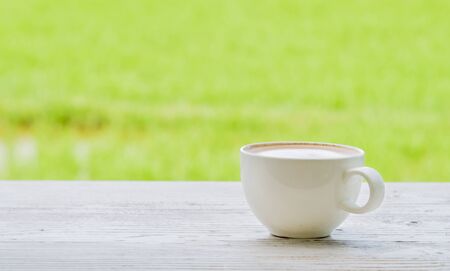Fresh coffee in the glass on the wooden floor white. Behind the green fields blur and poor light.の写真素材