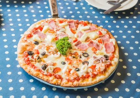 Hawaiian Pizza and Seafood In white plate placed on a blue and white striped fabric. The background is blurred and poor light.の写真素材