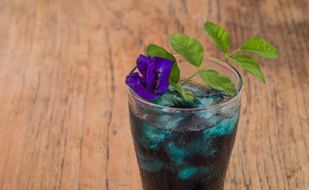 Butterfly pea water. Add ice, decorated with flowers and leaves lay on a wooden floor. Focus on the glass.の写真素材