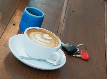 Coffee latte in white glass, car keys and tea on the table dark wood coffee focus.の写真素材