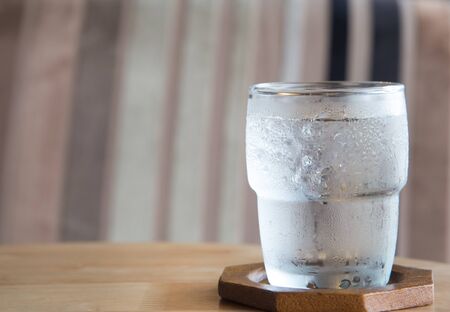 Glass of water placed on a wooden table.Behind the chintz chairs  blur.