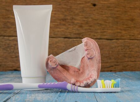 Denture mold,broken tooth,old toothbrushes and toothpaste placed on wooden floor.