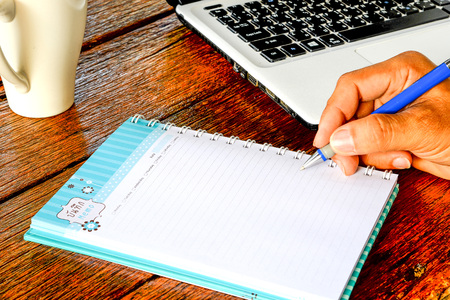 Coffee , Notebook , Laptop , Writing pen in hand,All place on Dark wooden desk top view.Copy space...