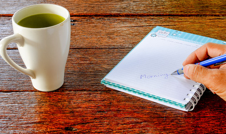 Coffee , Notebook , Morning writing pen in hand,All place on Dark wooden desk top view.Copy space for message.の写真素材